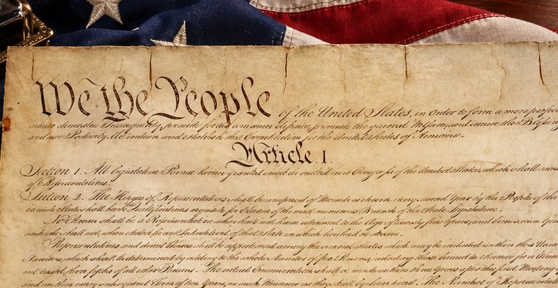 The preamble to the United States Constitution, beginning We the People, resting on an American flag